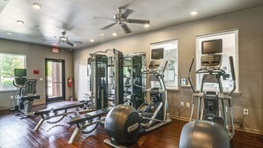 A gym with various exercise equipment, a ceiling fan, and windows with views of the outdoors.