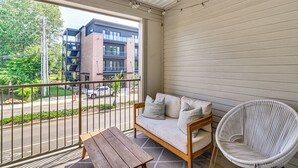 A balcony with a wooden table, a wicker chair, and a sofa with cushions.