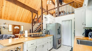 Eine geräumige Küche mit Holzbalkendecke, weißen Schränken, einem Edelstahlkühlschrank und einer Holz Arbeitsplatte.