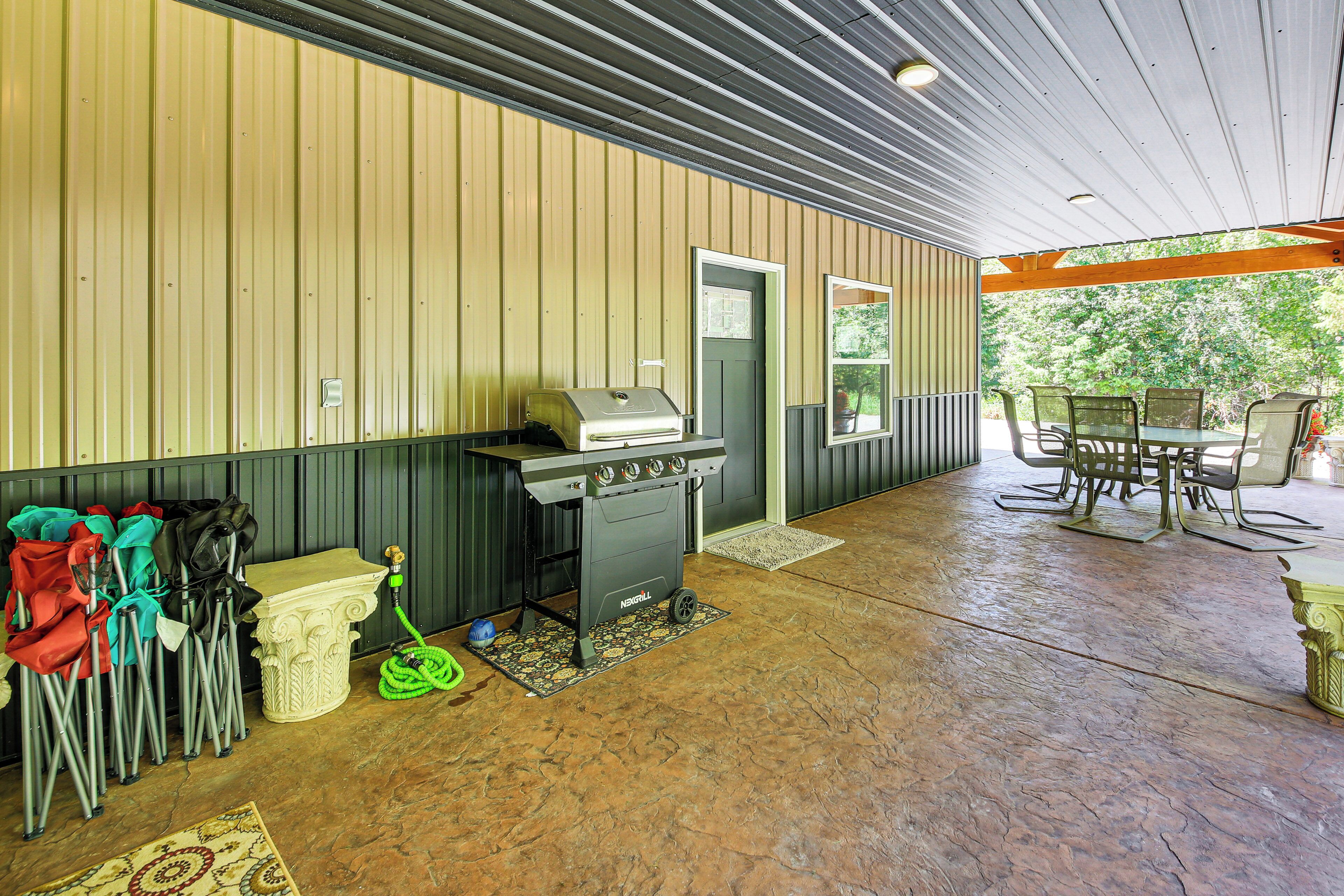 Un patio techado con una parrilla, mobiliario exterior y vistas a árboles.