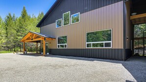 A modern building with a covered porch, large windows, and a gravel driveway. - Relax, Reconnect & Explore: Modern Idaho House! (Naples)