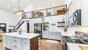 A spacious kitchen with a large island, white cabinetry, and a wooden staircase leading to an upper level. - Relax, Reconnect & Explore: Modern Idaho House! (Naples)