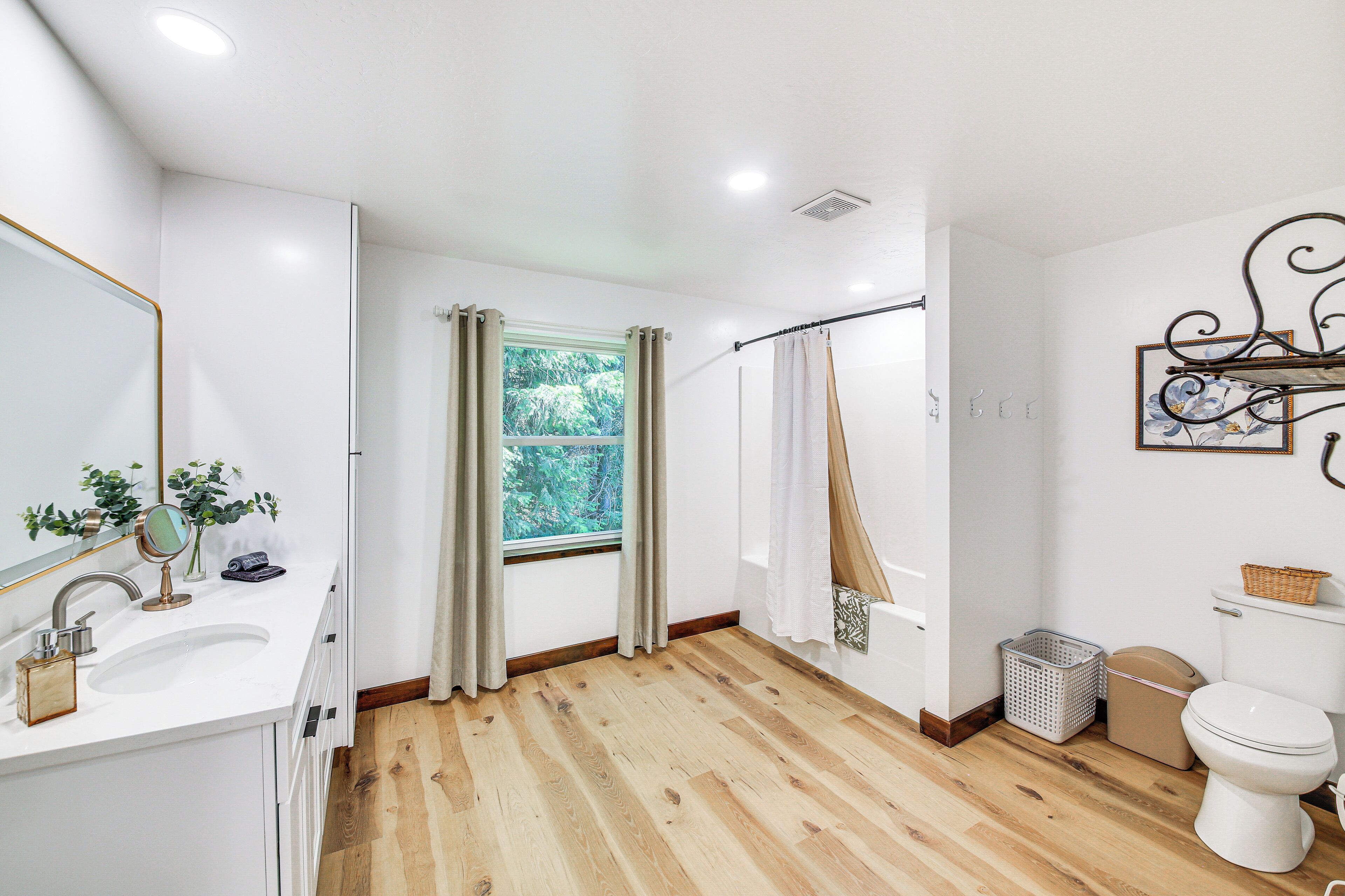 Ein Badezimmer mit Holzboden, weißen Armaturen, einem Fenster mit Vorhängen und einer Duschkabine.