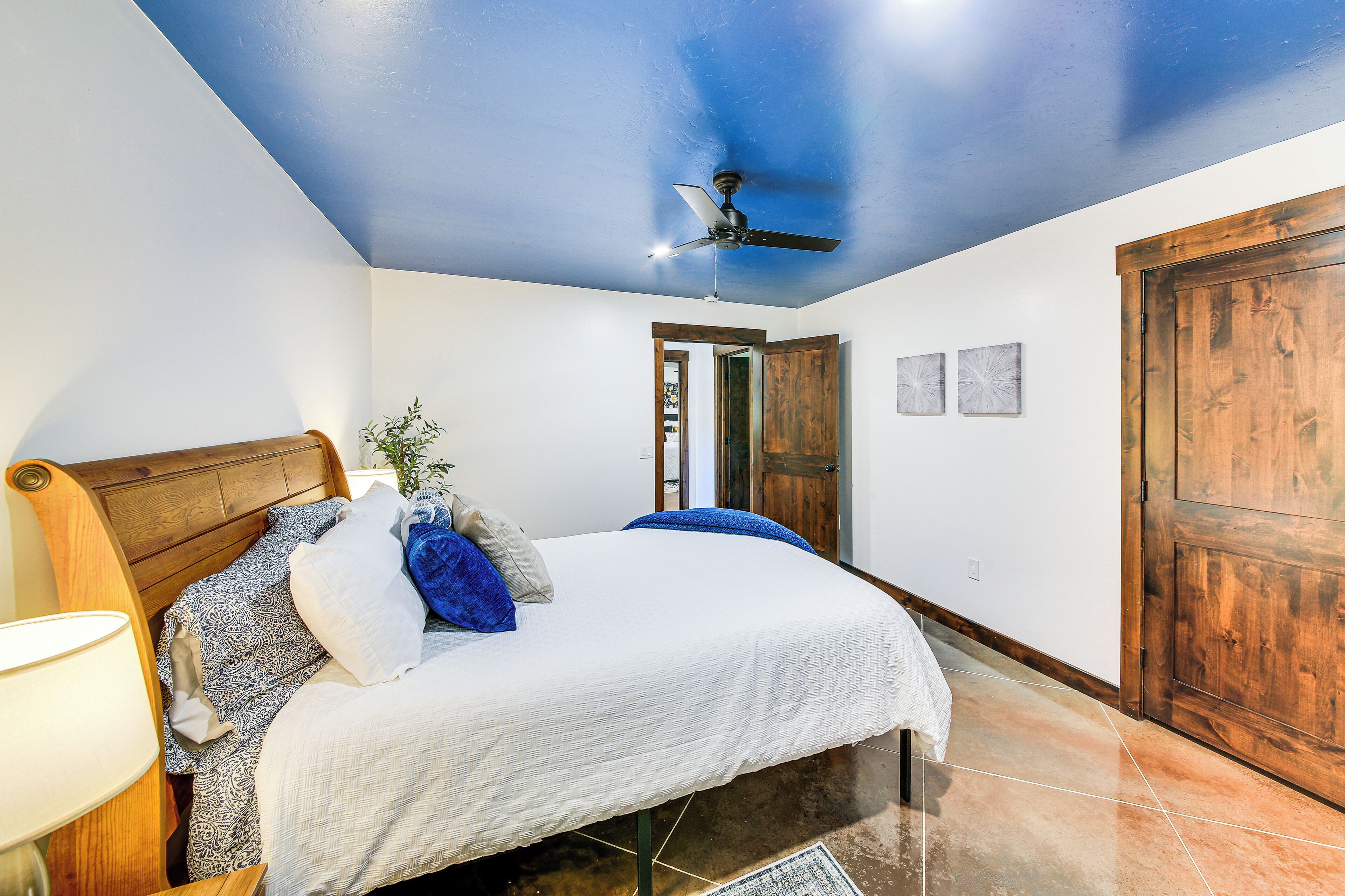 A bedroom with a bed, a ceiling fan, a wooden door, and a nightstand with a lamp.