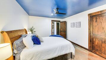 A bedroom with a bed, a ceiling fan, a wooden door, and a nightstand with a lamp.