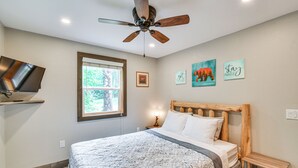 A bedroom with a bed, a ceiling fan, a TV, a window, and wall art. - Woodsy 20-acre Retreat w/ Hot Tub in Mancelona (Mancelona)
