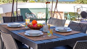 Une table à manger extérieure avec des chaises, un saladier rempli de fruits et un vase de fleurs.