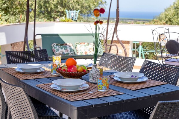 An outdoor dining table with chairs, a bowl of fruit, and a vase with flowers.