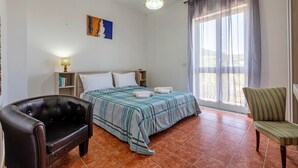 Une chambre à coucher avec un lit, une chaise, une lampe, un tableau et une fenêtre avec des rideaux.