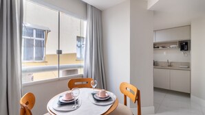 A dining area with a table set for two, a kitchen with modern appliances, and a view of the outside through a large window. - Beautiful Apart in Barra 110m From Beach Csf0202 (Salvador)