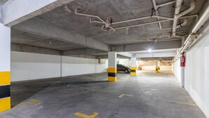 Un estacionamiento subterráneo de varios niveles con pilares de hormigón, columnas a rayas amarillas y negras, y extintores visibles.