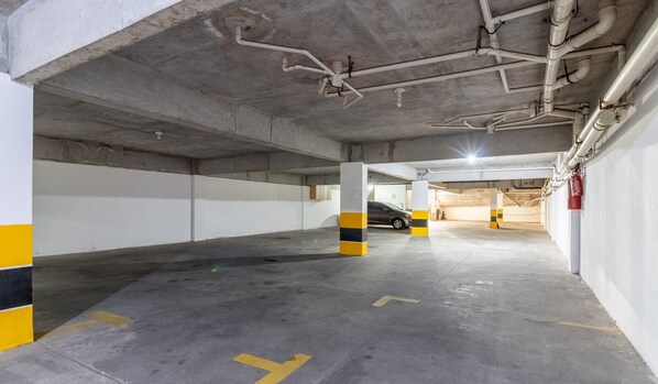 Ett underjordiskt parkeringsgarage i flera våningar med betongpelare, gul- och svartrandiga kolonner och synliga brandsläckare.