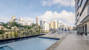 A rooftop pool with a city skyline in the background, surrounded by palm trees and lounge chairs. - Beautiful Apartment 500m From Shopping Csp1207 (Salvador)