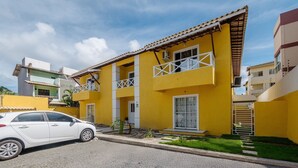 Un bâtiment jaune doté de balcons, une voiture garée devant, et un ciel dégagé.