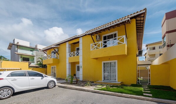 Un bâtiment jaune doté de balcons, une voiture garée devant, et un ciel dégagé.