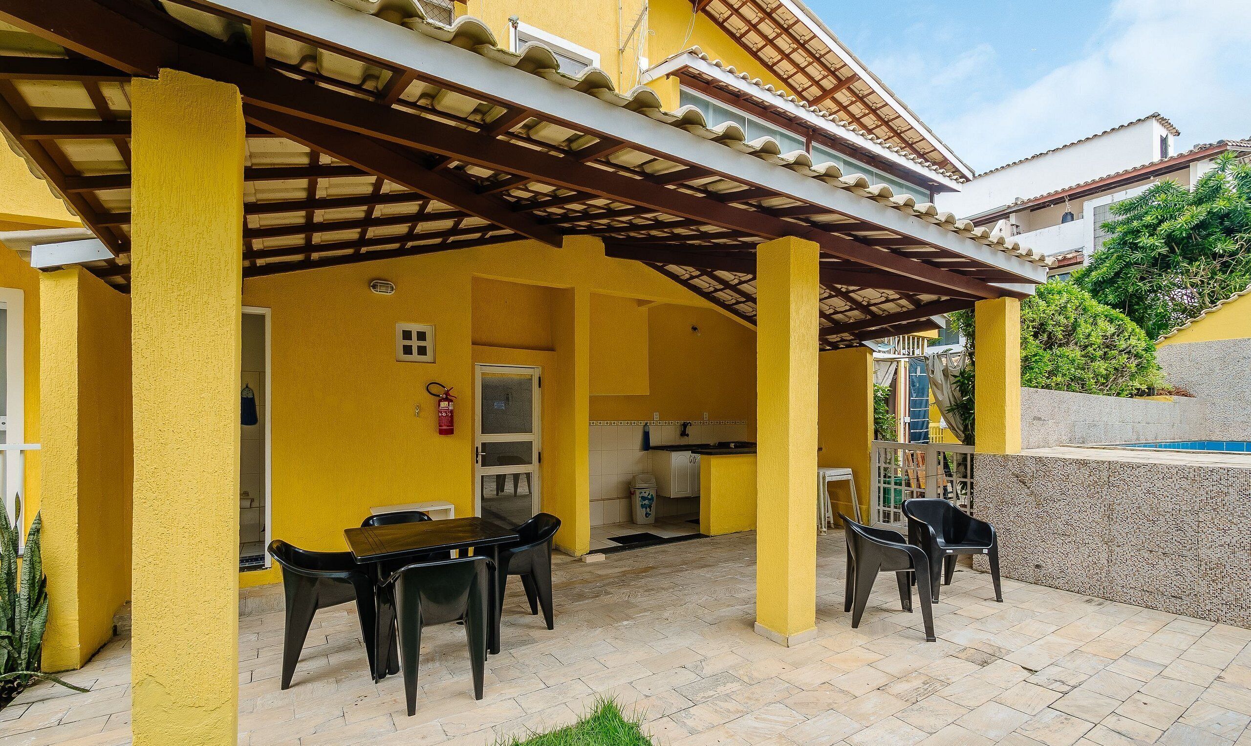 A yellow building with a covered patio area, a table with chairs, and a kitchen visible through an open door.