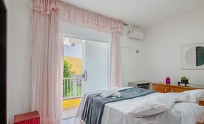 Ein Schlafzimmer mit einem Bett, einem kleinen Nachttisch aus Holz, einem Spiegel und einem Fenster mit Vorhängen.