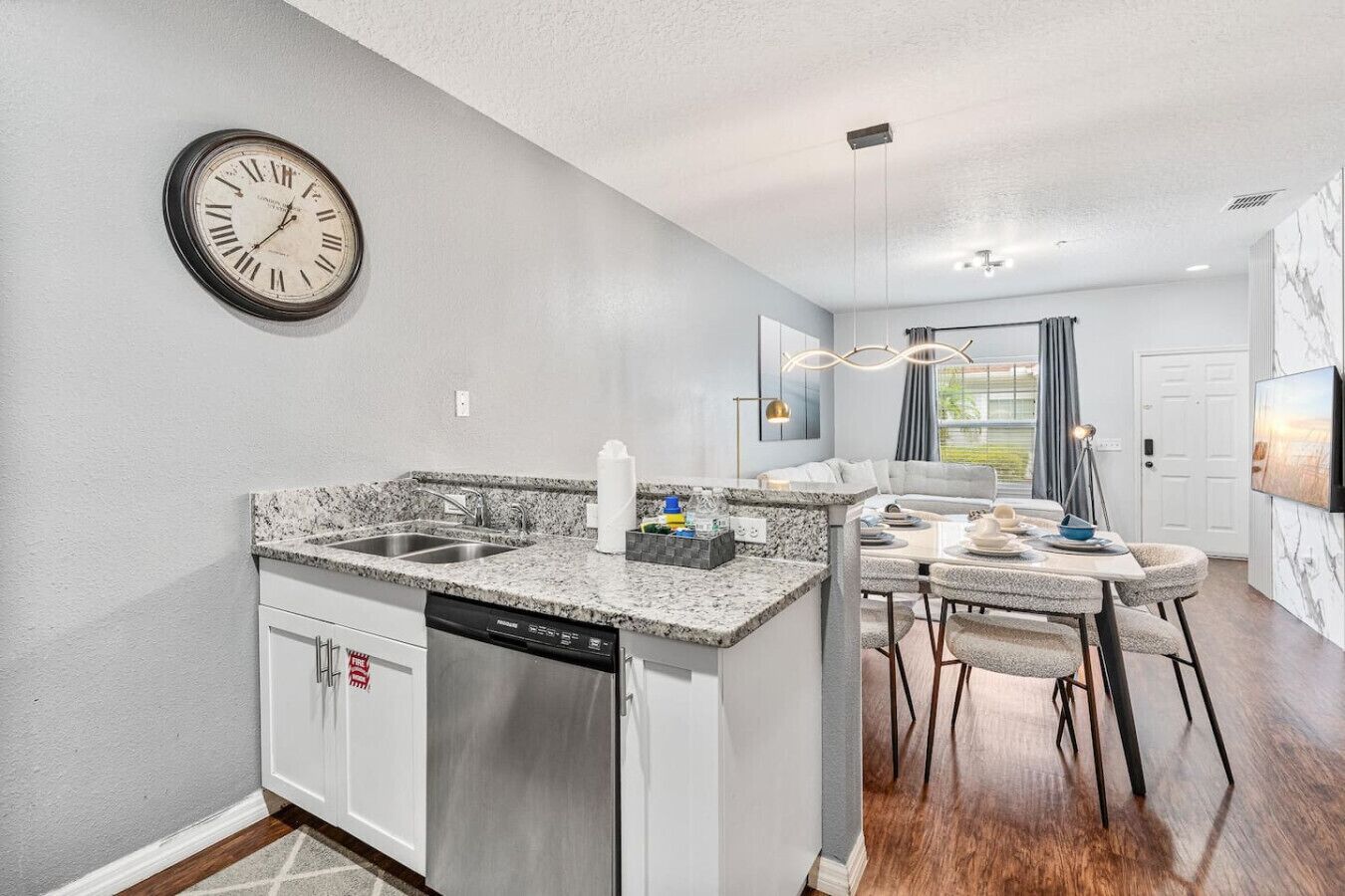 A modern kitchen with granite countertops, a dishwasher, and a dining area with a table and chairs.