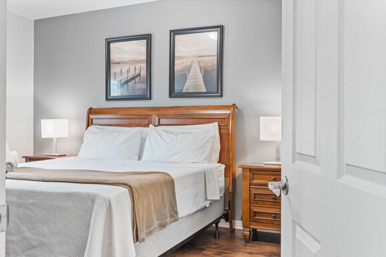 A neatly arranged bedroom with a wooden bed, two bedside tables with lamps, and two framed pictures on the wall.