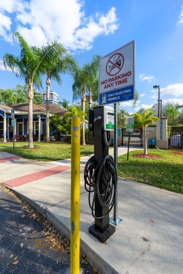 Una señal de prohibido estacionar, estación de carga para vehículos eléctricos y un edificio de fachada azul con palmeras.