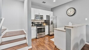 A modern kitchen with white cabinets, stainless steel appliances, and a clock on the wall.
