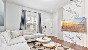 A modern living room with a sectional sofa, two round coffee tables, a patterned rug, and a large painting on the wall.