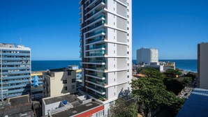 Un edificio de gran altura con varios balcones, vistas despejadas al mar y una mezcla de arquitectura moderna y más antigua al fondo.