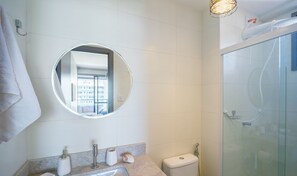 Ein Badezimmer mit rundem Spiegel, Toilette, Waschbecken und einer Duschkabine.