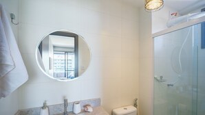 Un baño con un espejo redondo, inodoro, lavamanos y ducha con mampara de vidrio.