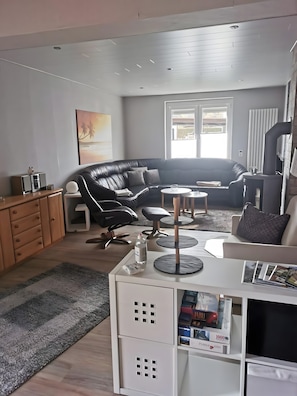 A modern living room with a black leather sofa, a white coffee table, a white cabinet with storage, and a large window providing natural light.
