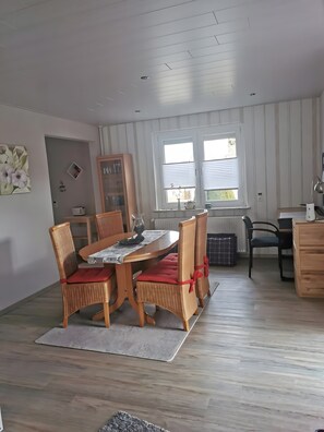 A dining area with a wooden table and wicker chairs, a cabinet, and a window with blinds.