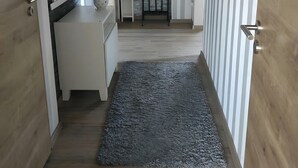 Een gang met streepmuren, een witte bank, een zwart metalen hek en een grijze vloerkleed.