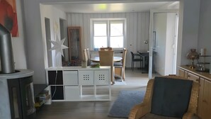 Een ruime woonkamer met een open haard, een eettafel, een rieten stoel en een ronde salontafel.