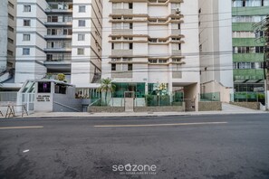 A multi-story residential building with balconies, a gated entrance, and a clear road in front.