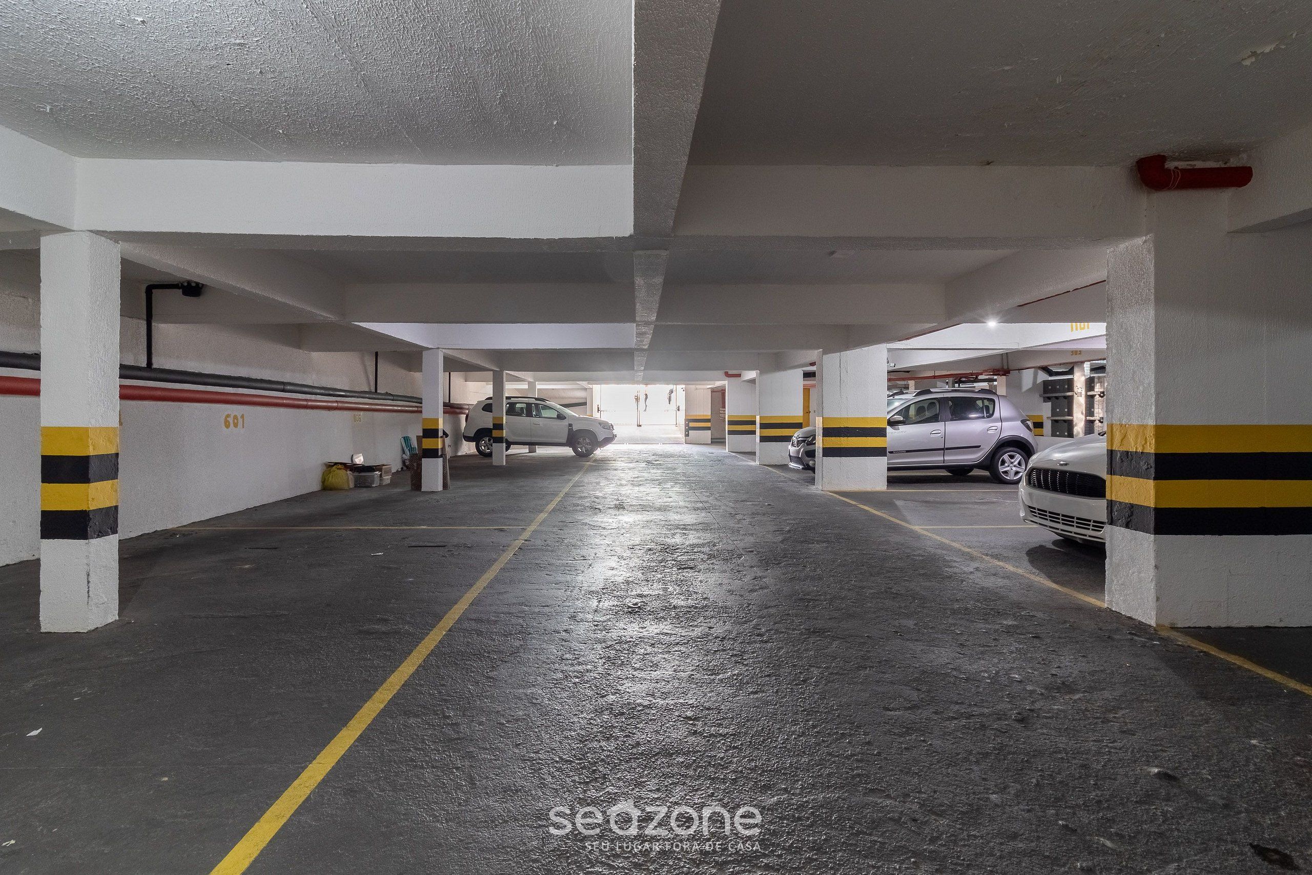 An underground parking garage with concrete pillars, yellow and black striped walls, and a wet floor.