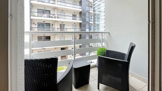 Un balcon doté de meubles en osier et offrant une vue sur un immeuble à plusieurs étages.