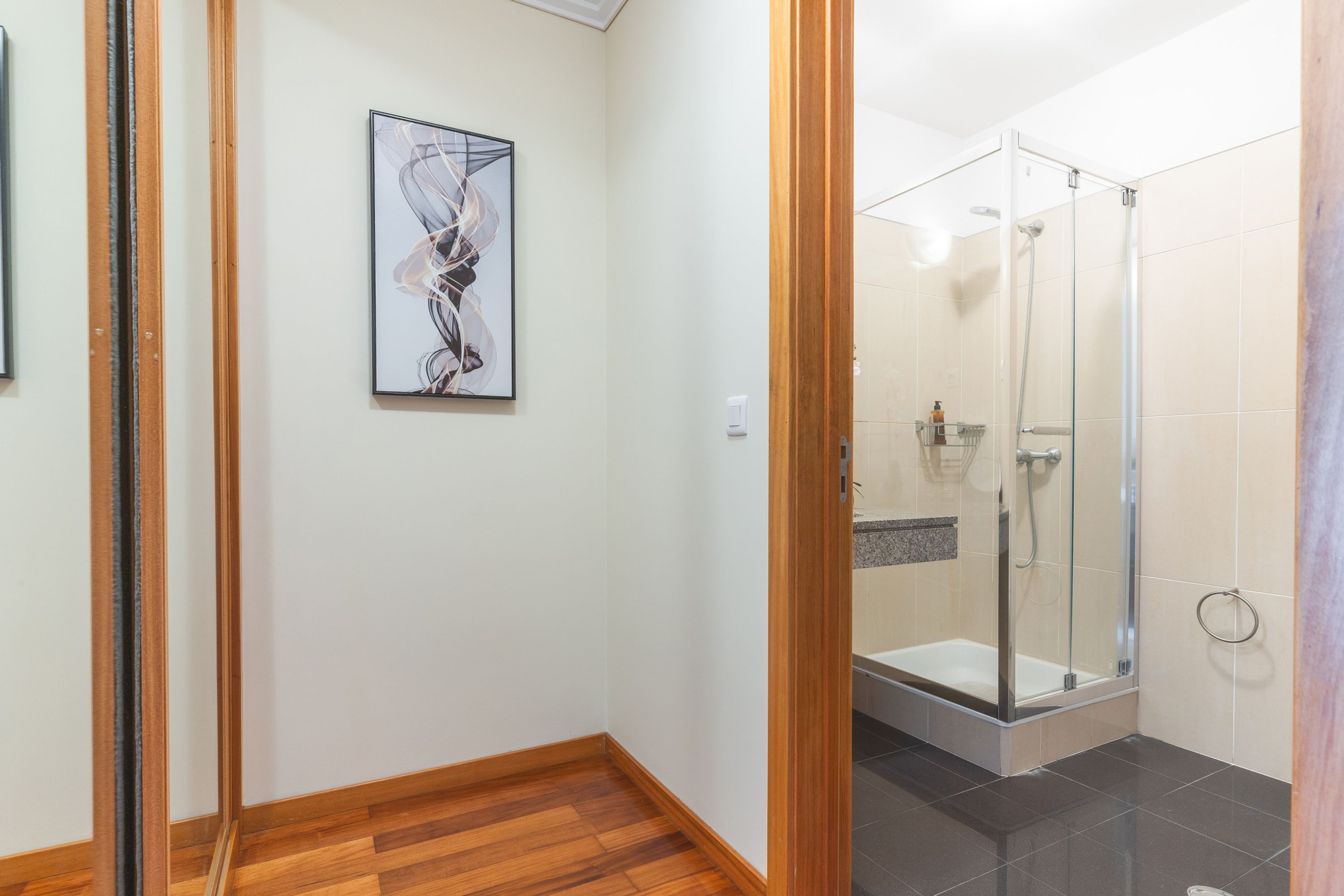 A modern bathroom with a glass shower enclosure, a wooden floor, and a framed abstract artwork on the wall.