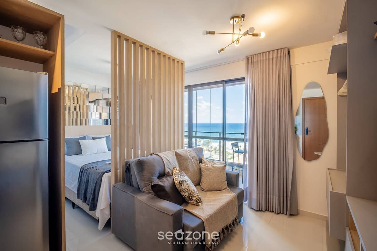 Ein modernes Schlafzimmer mit Bett, Sofa, großem Fenster und Meerblick.