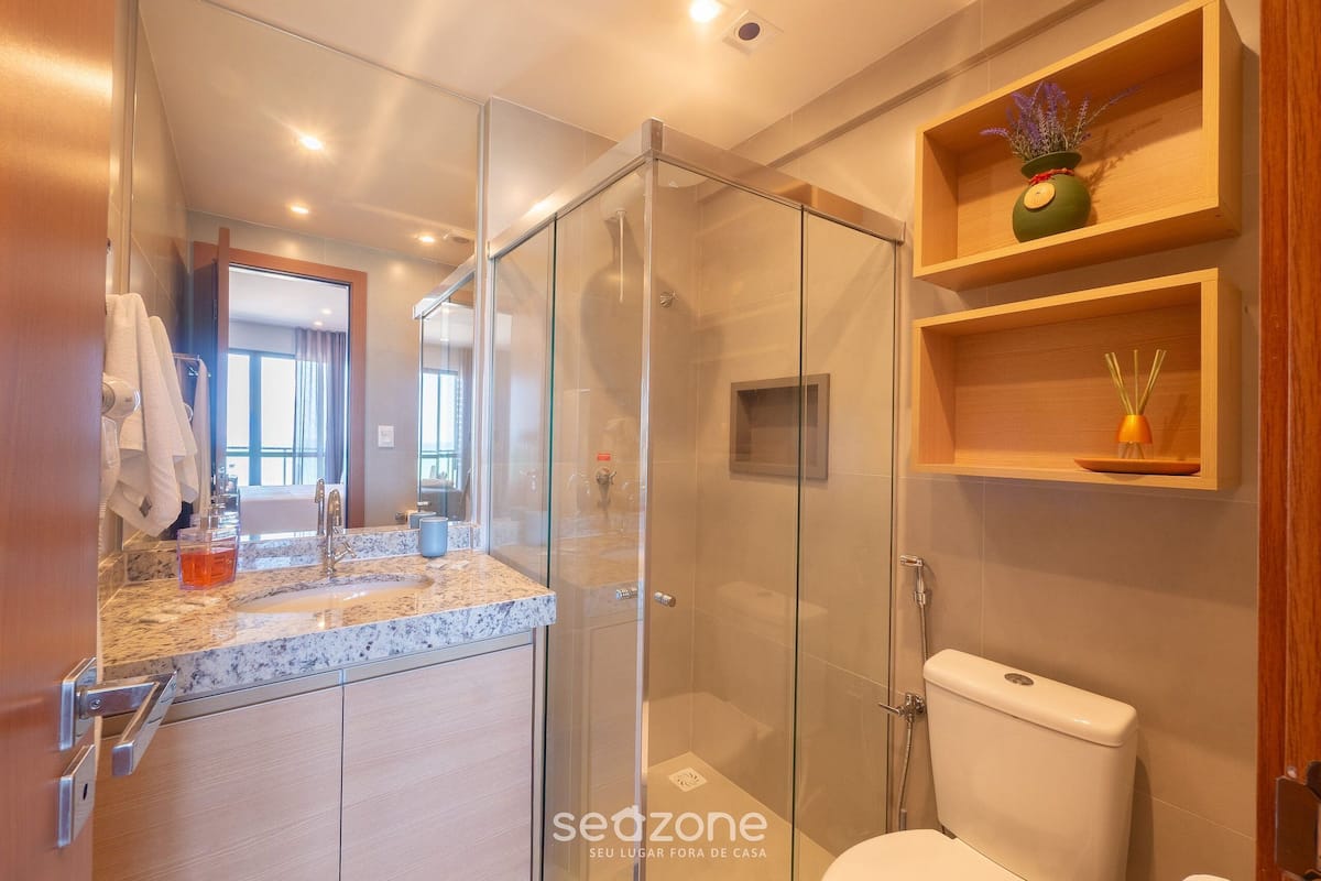 Ein modernes Badezimmer mit einer in Glas eingefassten Dusche, einem мрамоrn Waschtisch und Holzregalen über der Toilette.