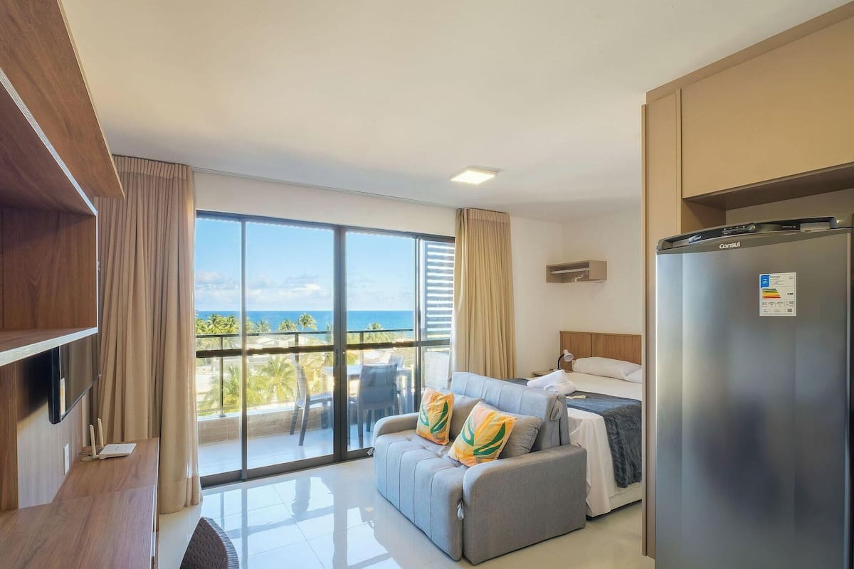 Ein modernes Hotelzimmer mit Balkon, einer Couch, einem Bett, einem Flachbildfernseher und einem Kühlschrank.