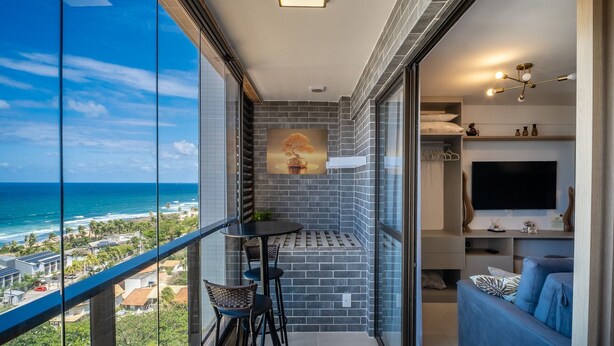 Een balkon met uitzicht op de oceaan, een kleine tafel met stoelen, een televisie en een modern interieur.
