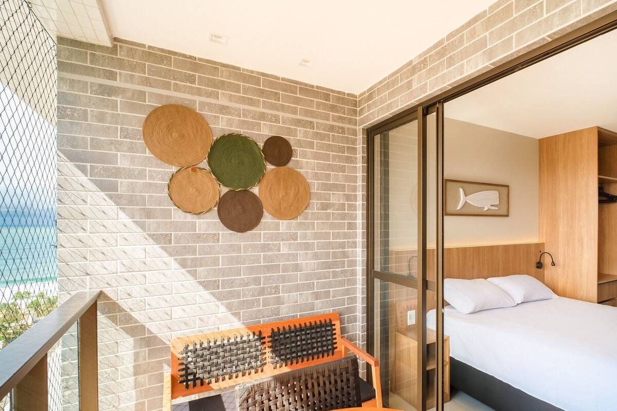 Ein modernes Hotelzimmer mit Backsteinwand, einem Bett mit weißen Leinen, einem Holzschrank und einem an der Wand befestigten Regal mit gewebten Matten.