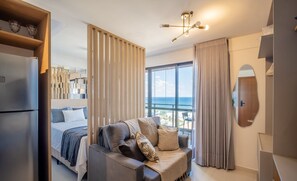 A modern hotel room with a bed, a sofa, a large window with a view, and a ceiling light fixture. - Stay Just Steps From Itapua Beach, With Pool and gym - RGF (Salvador)