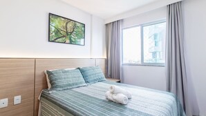 A modern hotel room with a large bed, a view of the city through a window, and a painting on the wall. - Beautiful Apartment in Salvador Rmo0602 (Salvador)