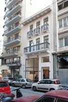 Un edificio de varios pisos con balcones, un letrero de hotel visible y automóviles estacionados.
