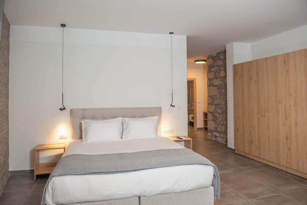 A bedroom with a large bed, a wooden wardrobe, and a stone wall.