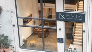 L’entrée d’un hôtel, avec une grande porte vitrée, une enseigne indiquant « HÔTEL EVIA OMONIA » et un escalier menant à l’intérieur.
