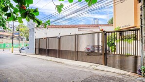 A gated residential area with a metal fence, a parked car, and a building with a tiled roof. - Modern Apartment 1km From Ondina Beach Slo0301 (Salvador)