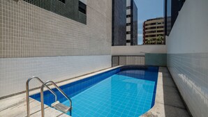 Une piscine avec un escalier en métal, entourée de murs recouverts de carreaux et d’une rambarde en métal.