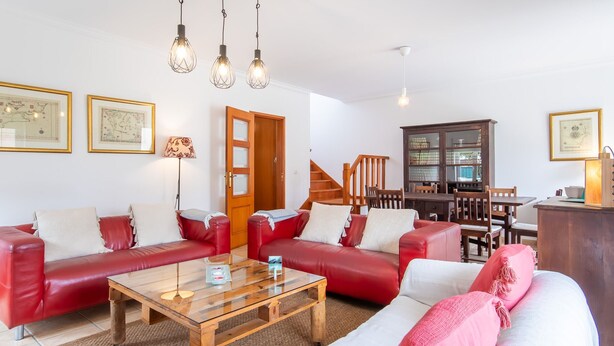 Una sala de estar con sofás de cuero rojo, una mesa de centro de madera y una escalera que lleva a un comedor.